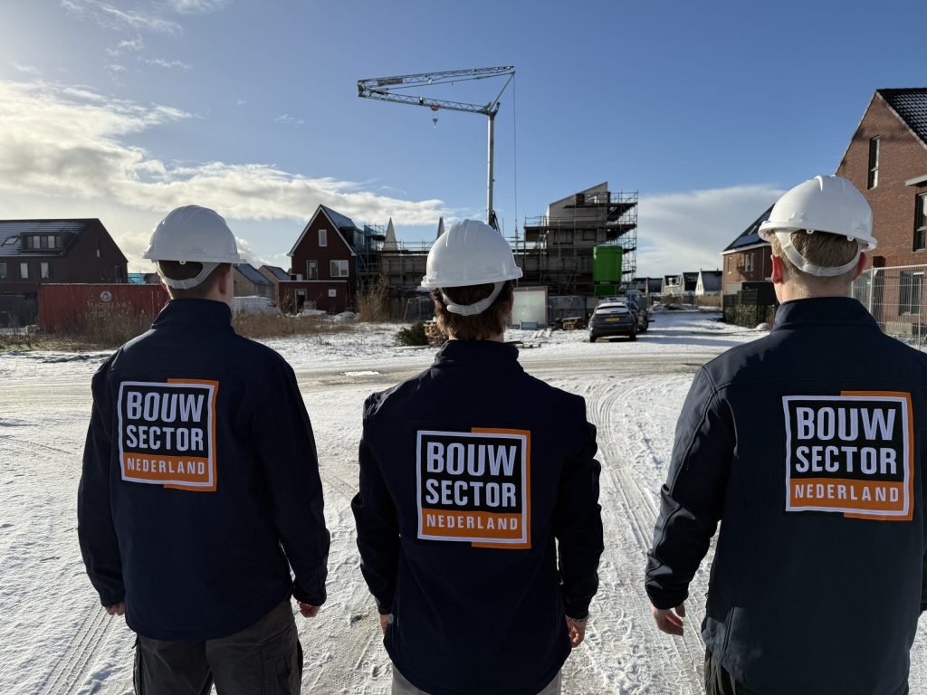 Drie vakmensen van Bouwsector Nederland met witte helm op een besneeuwde nieuwbouwstraat
